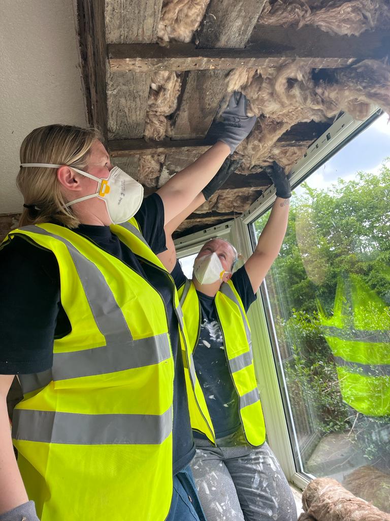 A woman with a mask on who is putting in a window with draught proof.