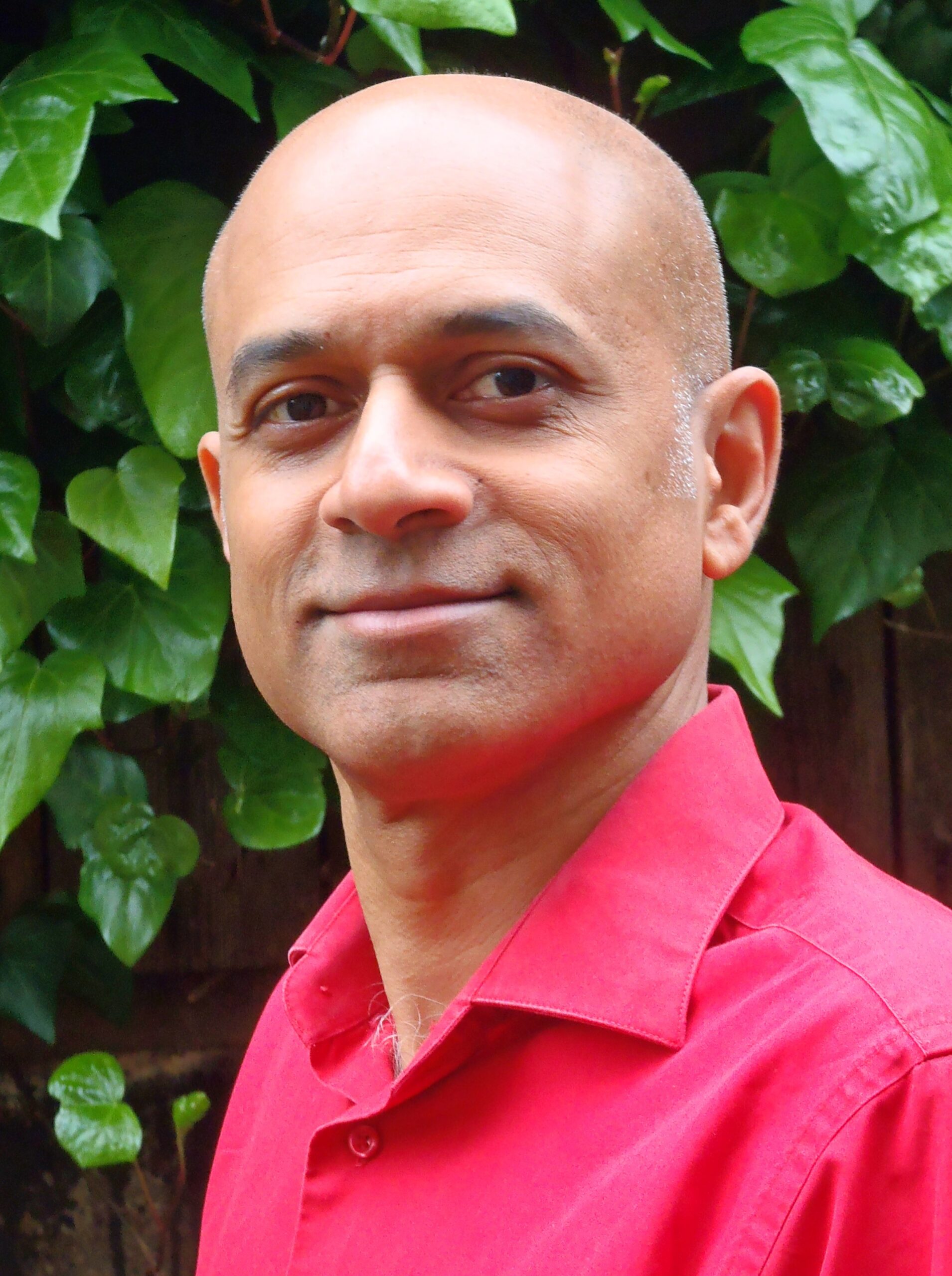 Photo of man in a pink collared shirt standing in front of a bush