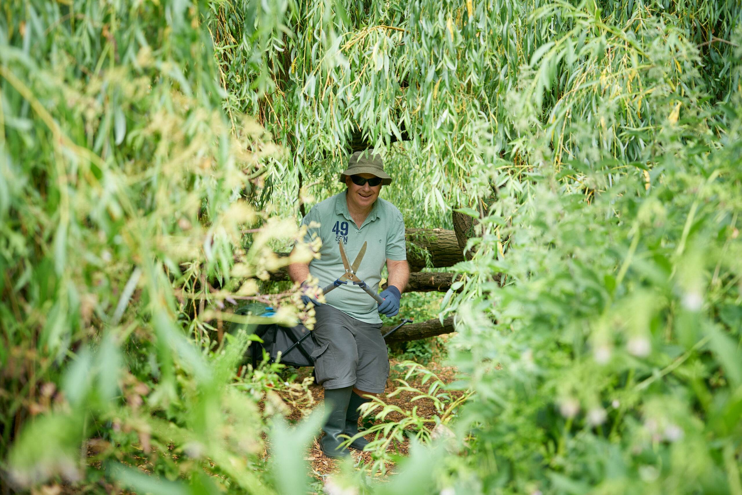 A man poses with gardening tools between trees.