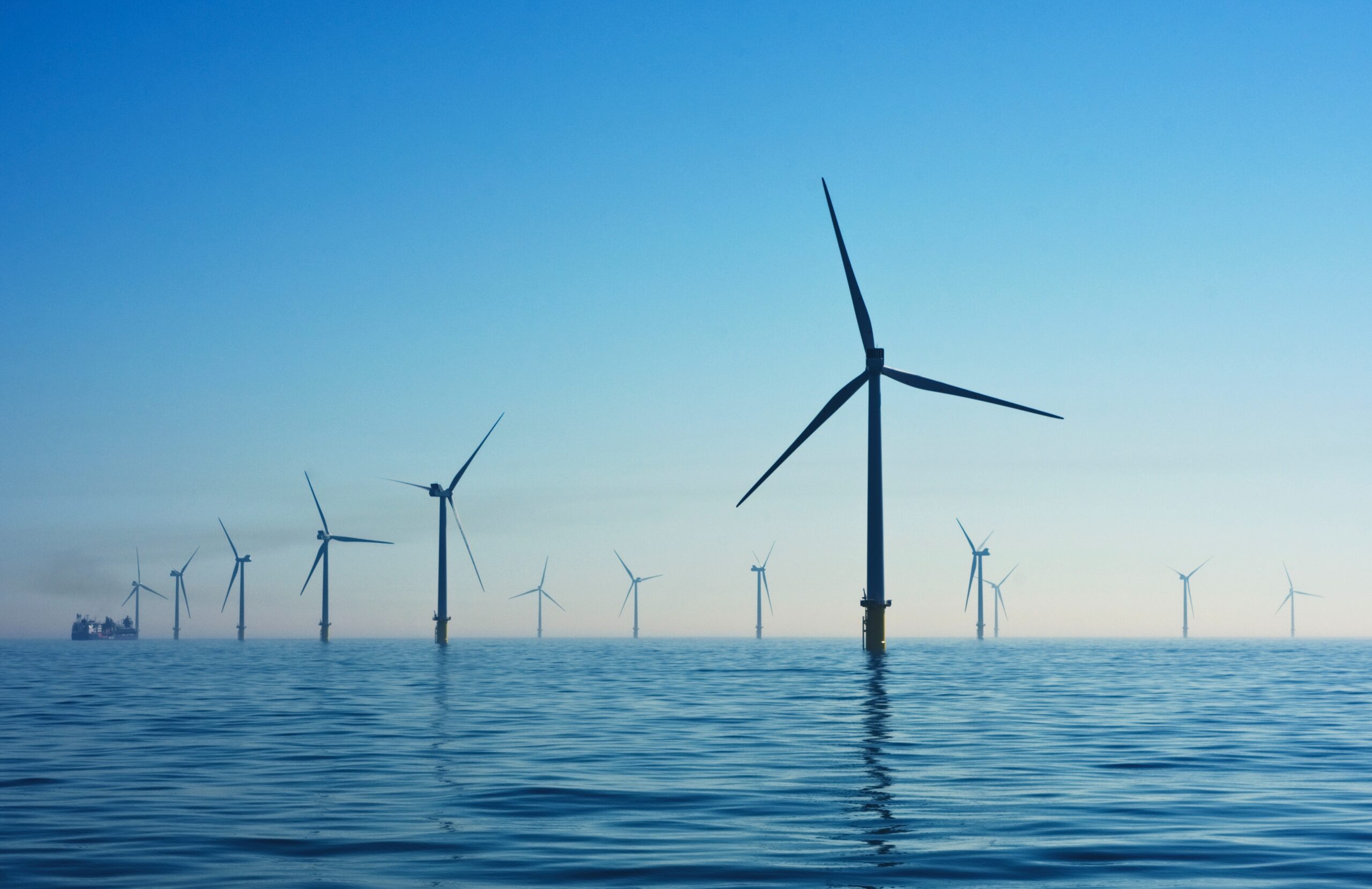 A collection of offshore wind turbines scattered around an ocean scene at dusk.