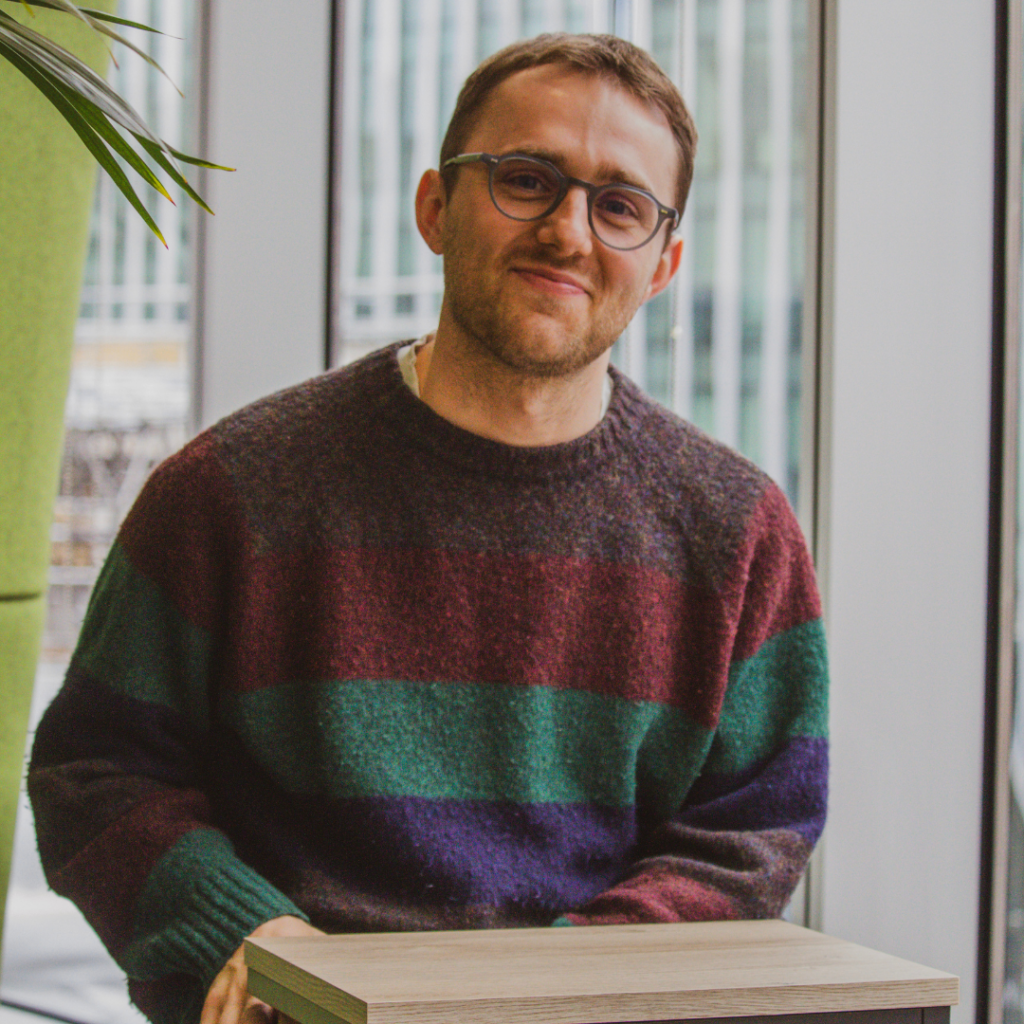 Man with glasses wearing a stripey jumper sitting and smiling