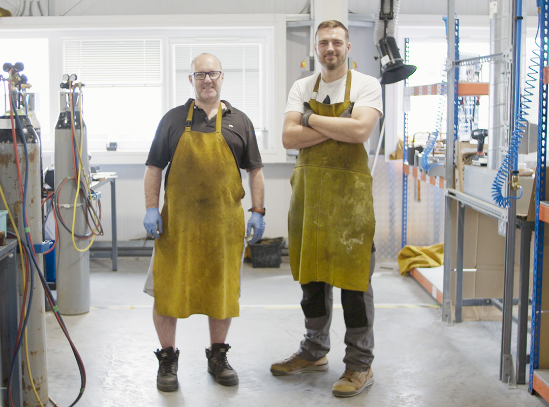 Two men wearing aprons standing staring at the camera