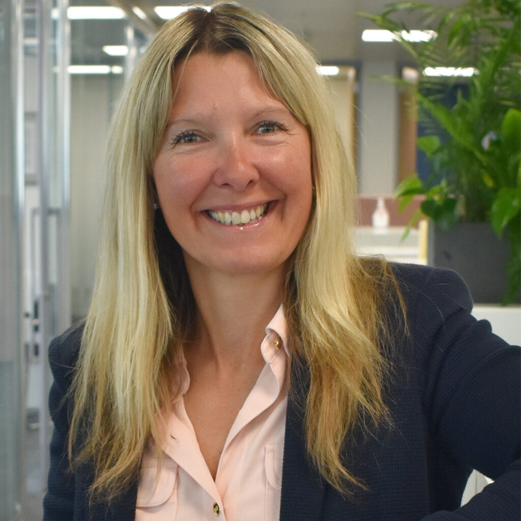 Woman with blond hair wearing a black suit jacket smiling at the camera