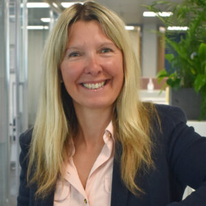 Woman with blond hair wearing a black suit jacket smiling at the camera
