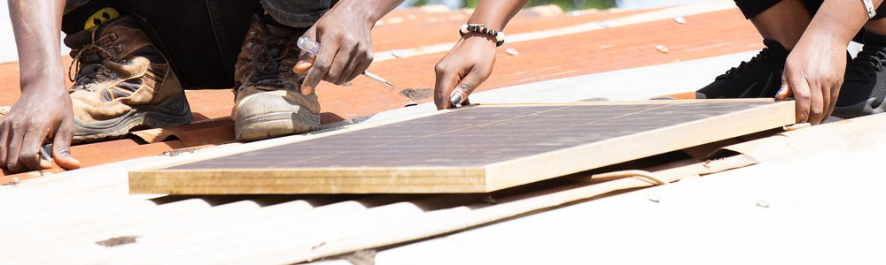 Two people are installing a solar panel on a home in a refugee settlement.