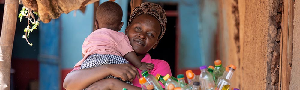 A woman holding her young child smiles at the camera in a refugee settlement.