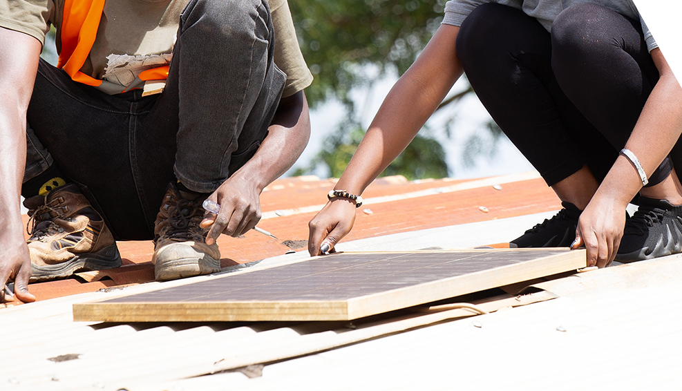 A refugee led organisation is installing a solar panel on a roof.