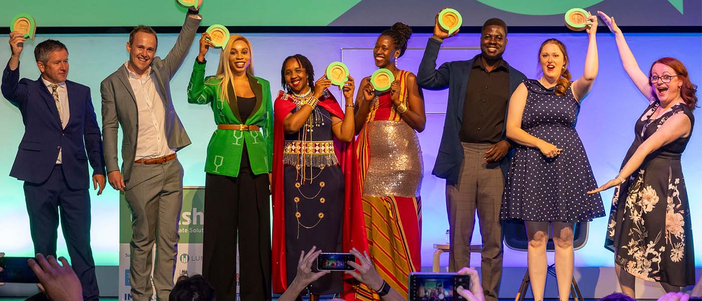 The 2024 Ashden Award winners are stood on stage cheering whilst lifting their trophies in the air.