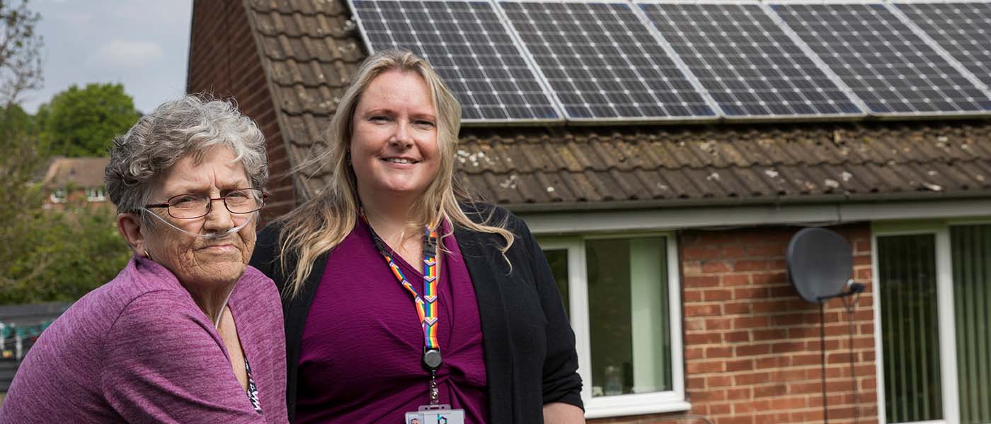 A home owner is stood with a local council manager in front of her home which has newly installed solar panels on it.