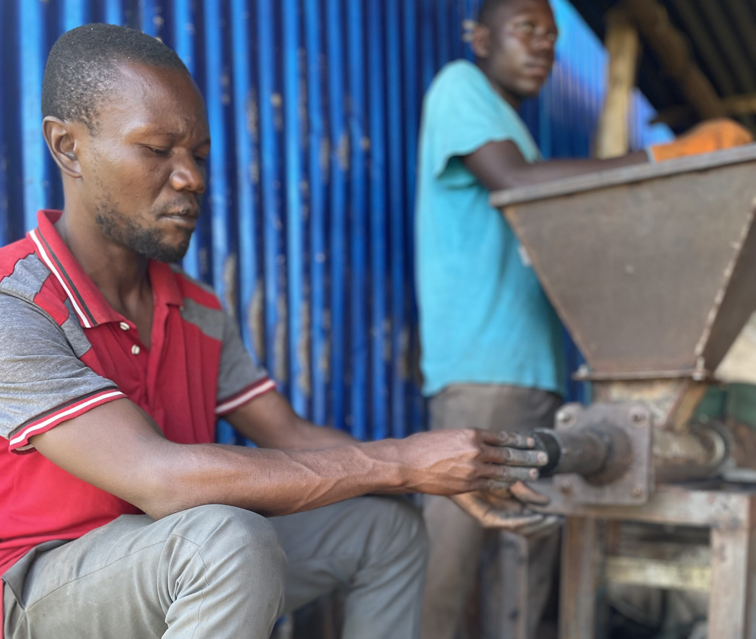 A refugee from Live in Green is sat on a stool collecting sustainable fuel from a machine. The fuel is made from waste produce.