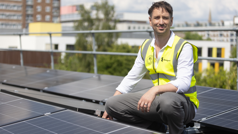The CEO of Emergent Energy smiling next to solar panels on a roof in Hackney