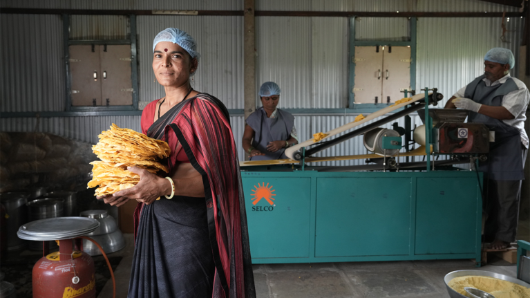 A woman who works for Selco standing with pumpdums staring at the camera
