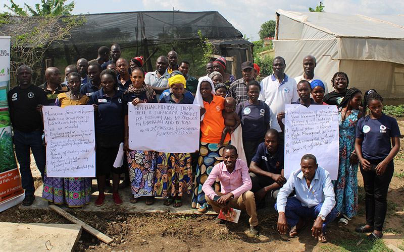 A community group supported by Bio Energy Umbrella Association of Kyangwali are gathered in front of the camera holding up signs.