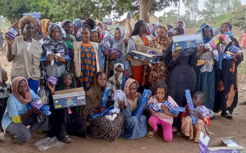 A group of woman and children who are supported by South Sudanese Women Building Association are gathered together and are smiling at the camera.