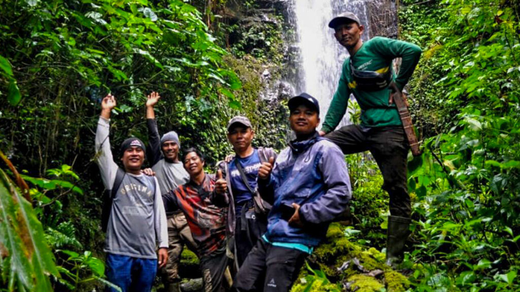 A group of people waving their hands in the air smiling in front of a waterfall in a forest