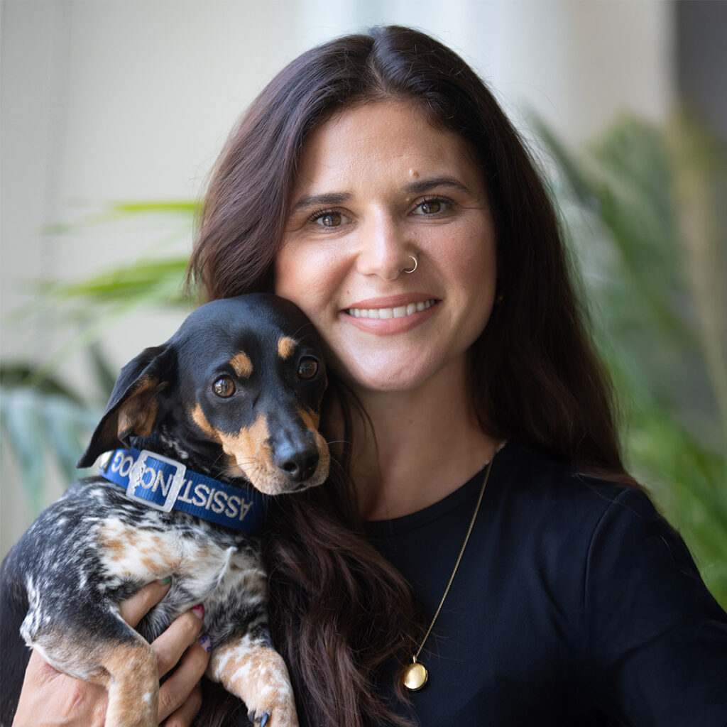 Woman with brown hair smiling with her assisant dog.
