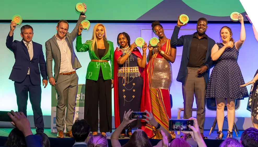 The Ashden Awards 2024 winners stand on stage cheering whilst lifting the trophies to the sky.