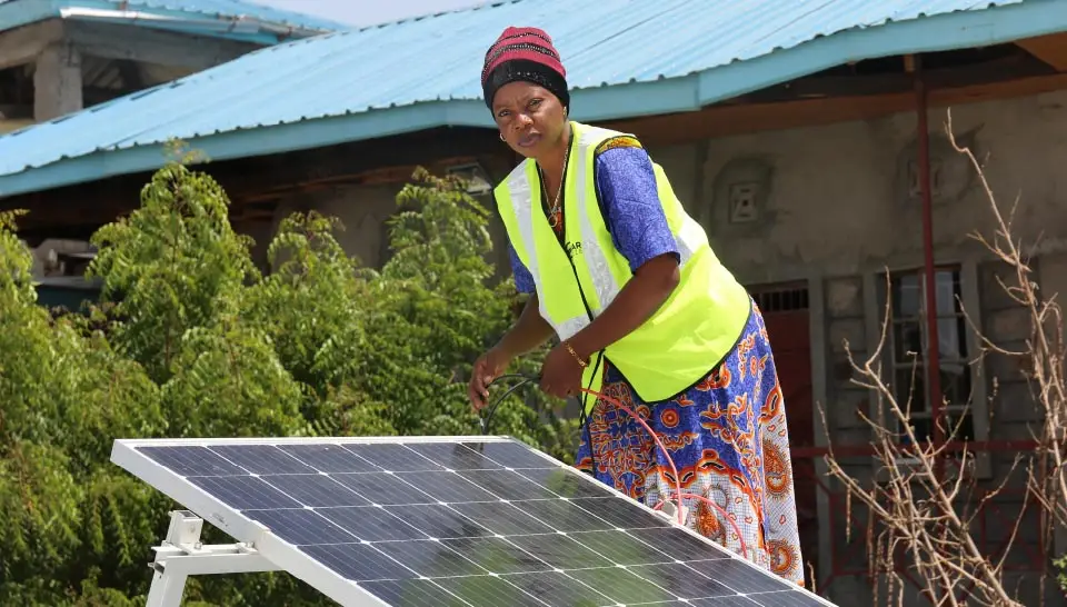 A woman in Sub-Saharan Africa is installing a solar panel.
