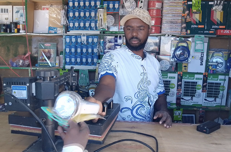 A small business owner in a refugee settlement, supported by Ashden's Transforming Humanitarian Energy Access program, is handing over a solar light to a customer.