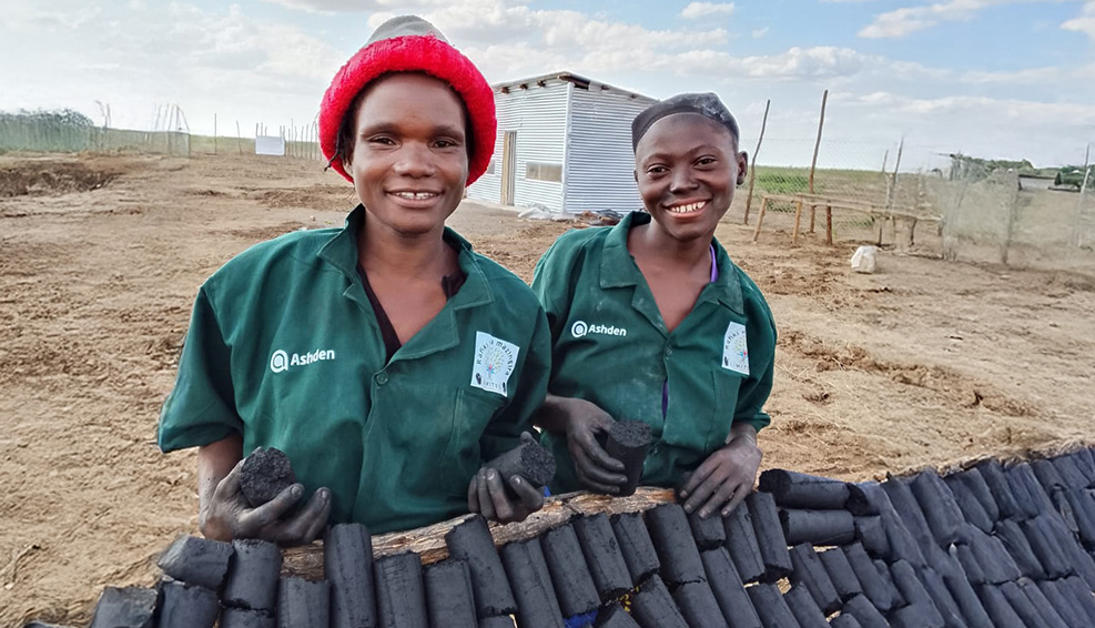 Two women are stood in front of clean energy briquettes that they have made.