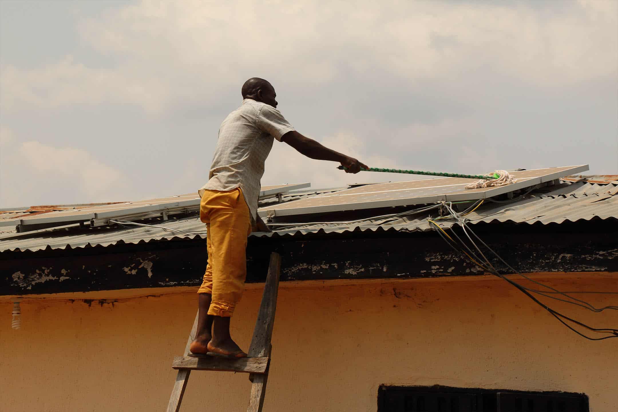 A man in Africa is cleaning roof top solar panels that have been installed as a clean energy solution.